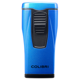 A metallic blue Colibri Monaco lighter with triple-jet flames and a black ignition button, featuring the brand name "Colibri, Est. 1928" near the base, is displayed against a white background.